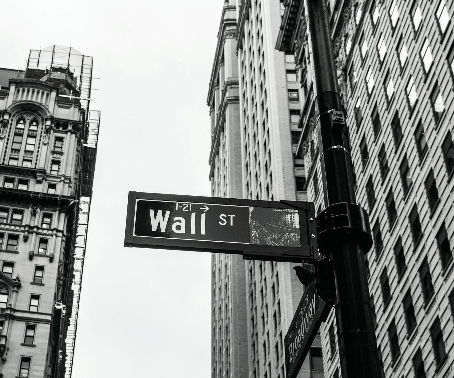 A Wall St street sign between old stone buildings, in black and white.